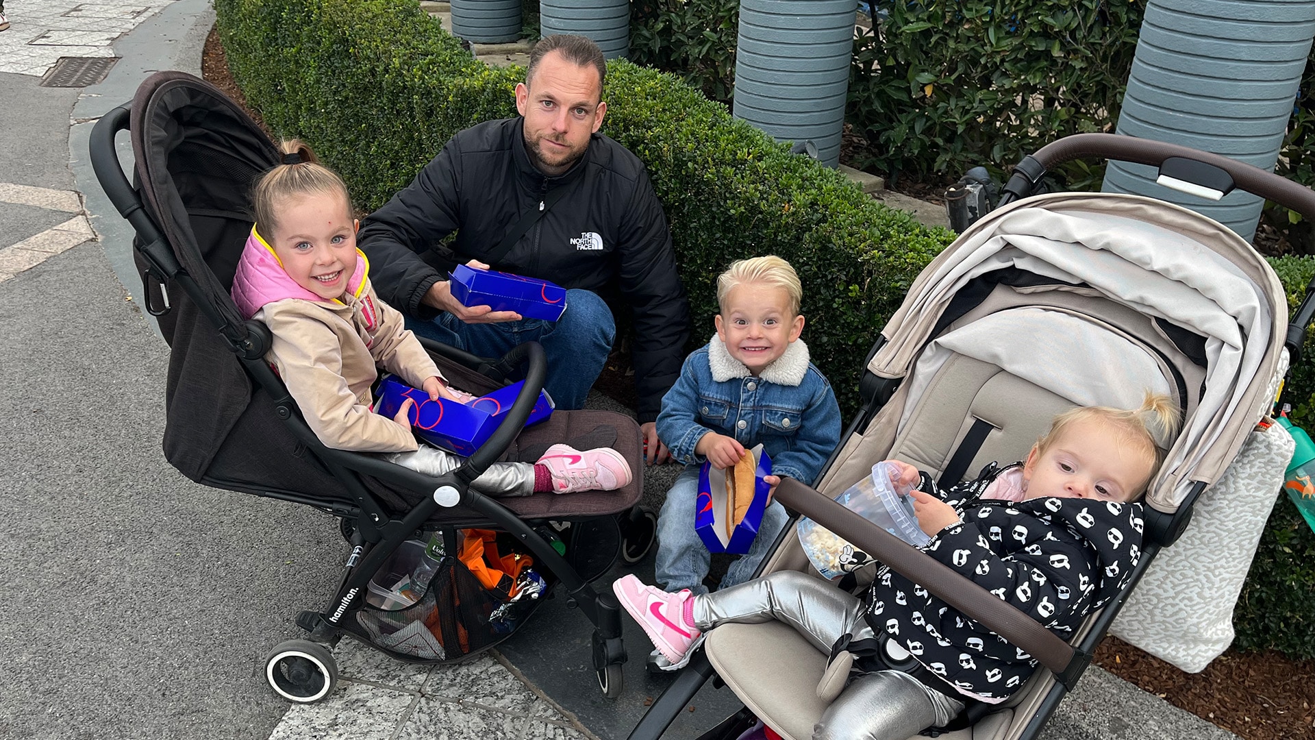 Papa en 3 kindjes zitten op een stoepje in het Walt Disney Studios Park en ze eten Hotdogs
