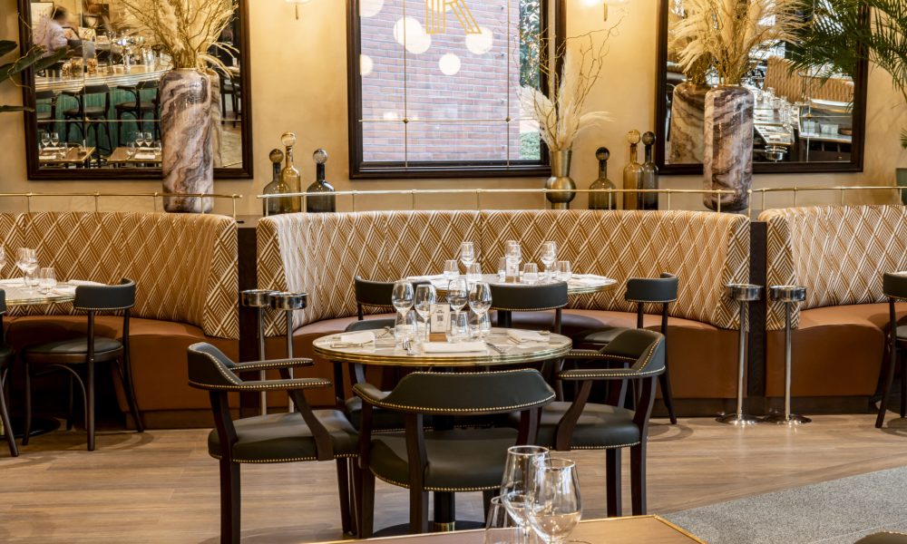 De sfeervol verlichte ingang en het terras van Brasserie Rosalie in Disney Village bij schemering.